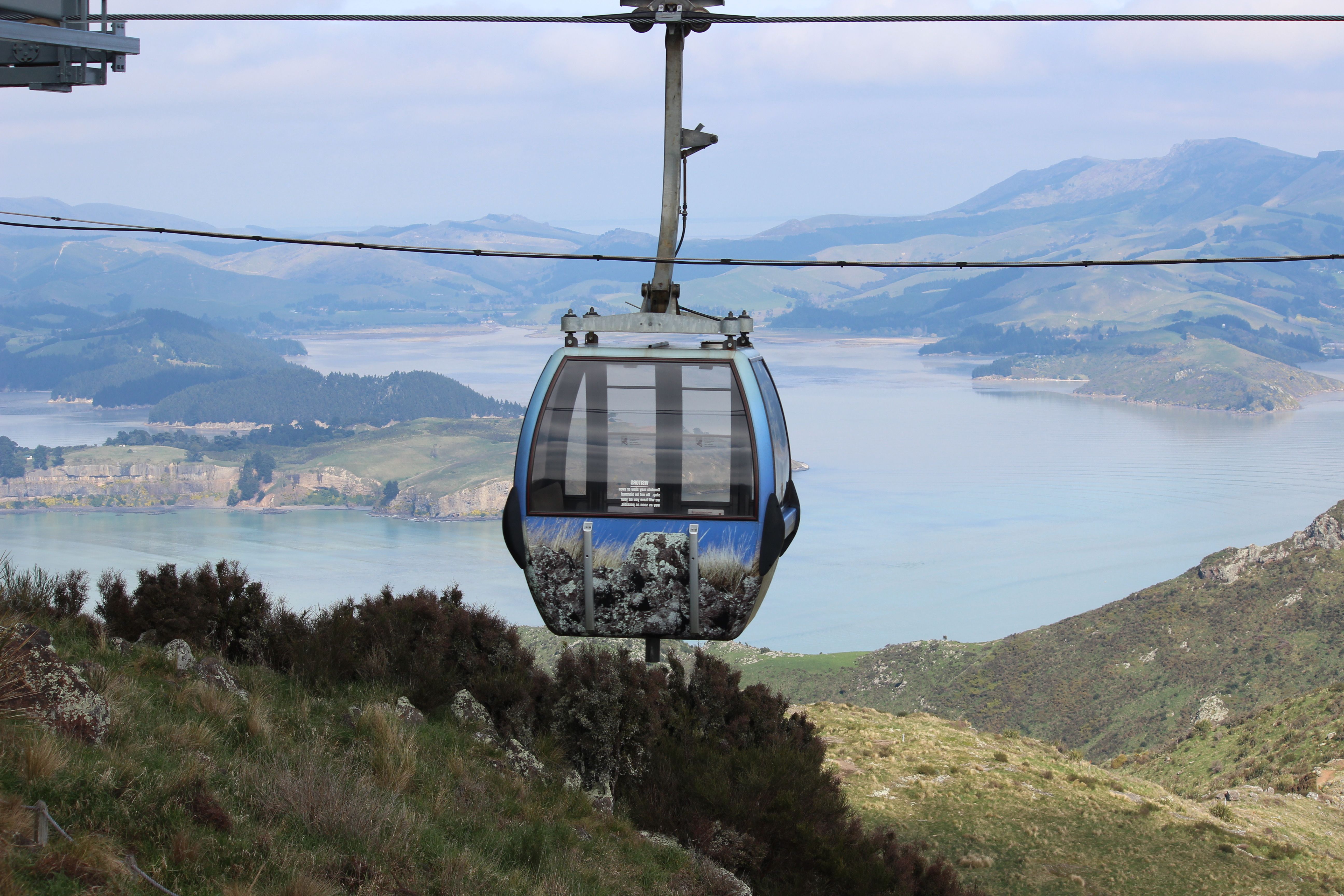 A cable car suspended over a lush, scenic landscape with a view of the coast.